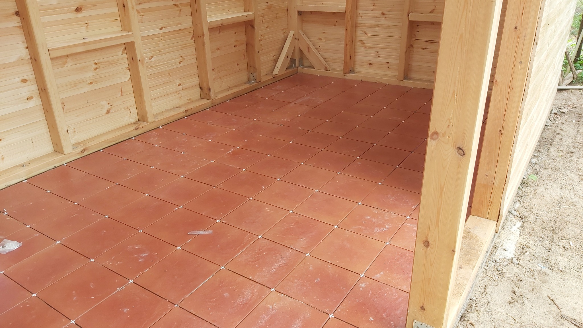 Podłoga w drewnianej altanie wyłożona terakotą z widocznymi krzyżykami dystansowymi, w trakcie układania.