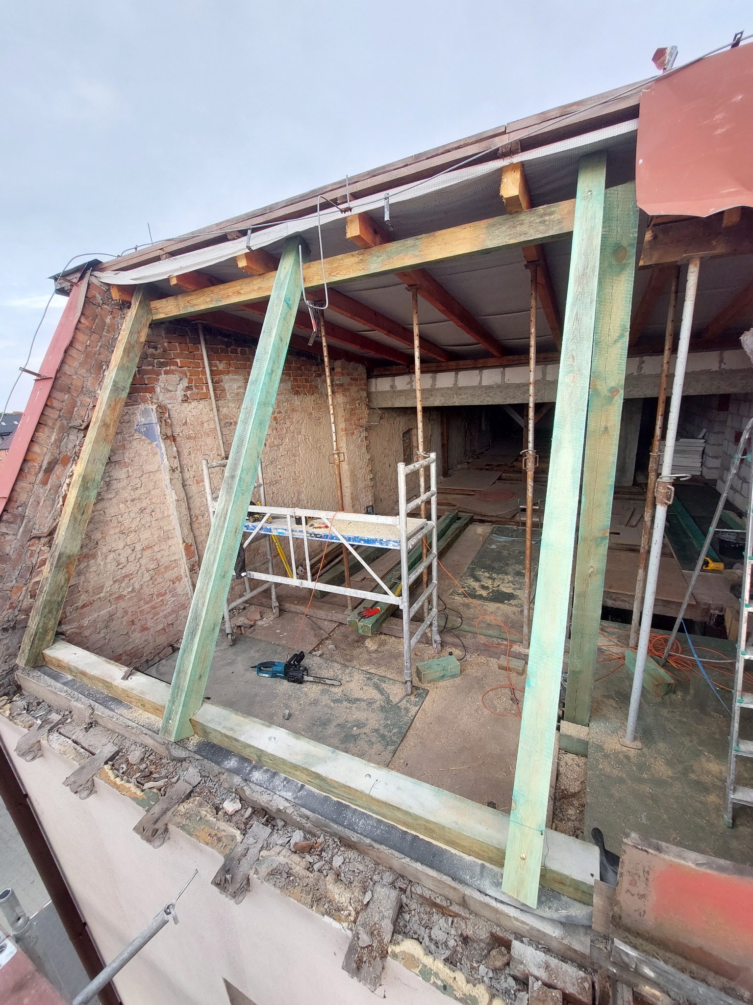 Konstrukcja drewniana poddasza w trakcie remontu, widoczne rusztowanie, cegły i narzędzia, częściowo zdemontowany dach.