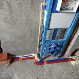 Stelaż podtynkowy WC w trakcie montażu, widoczne rury wodne w izolacji z pianki montażowej, surowa ściana w tle.