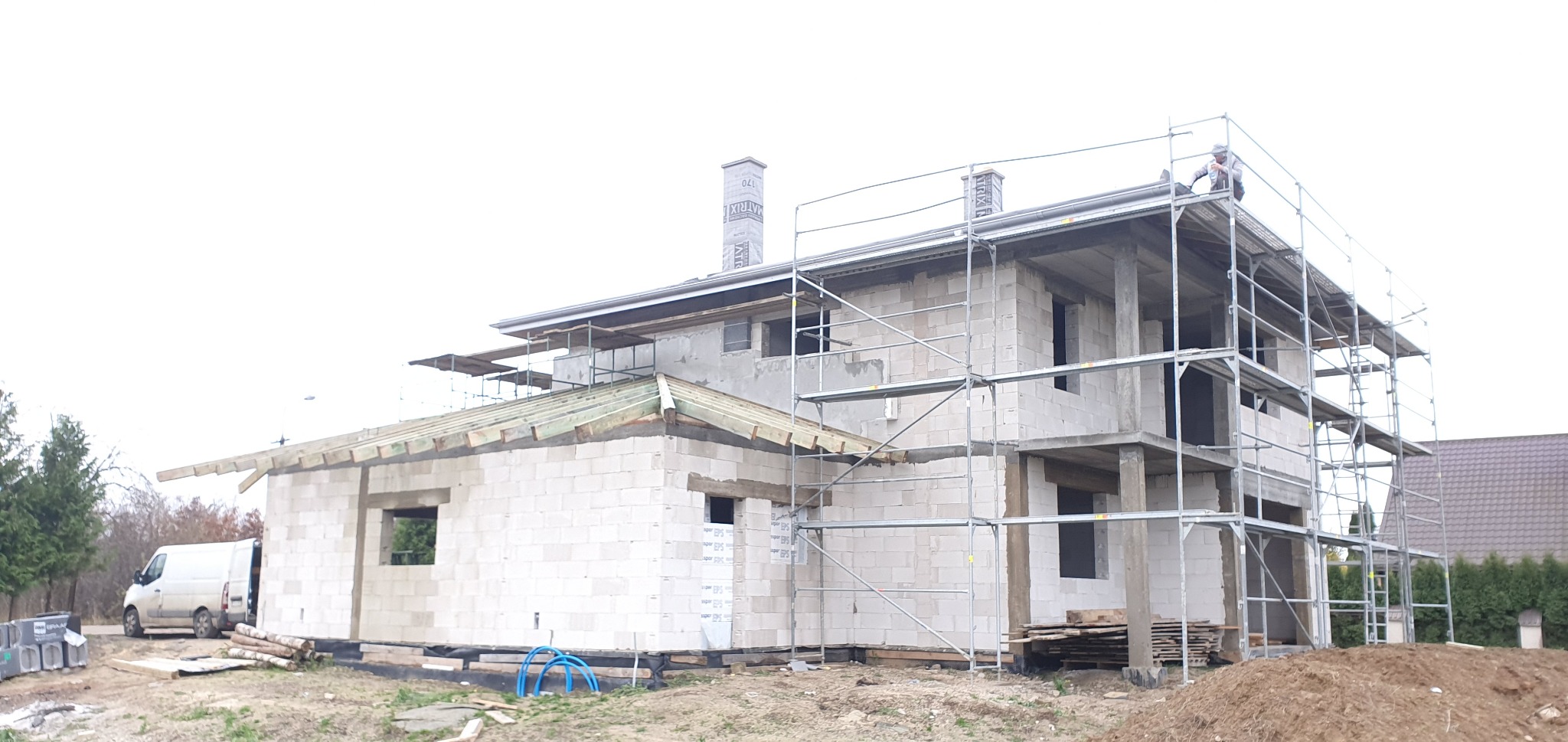 Budowa domu z pustaków: widoczna więźba dachowa, rusztowania i pracownik na dachu