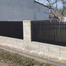 Łukasz Binkowski - Nowoczesne ogrodzenie z betonowych bloczków i pionowych, metalowych sztachet w kolorze grafitowym, z widoczną zabudową w tle.