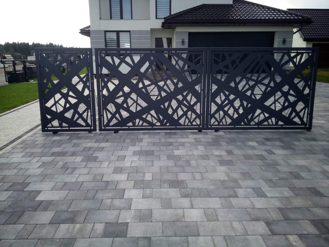Nowoczesna, metalowa brama wjazdowa z abstrakcyjnym, geometrycznym wzorem na tle domu jednorodzinnego z garażem.