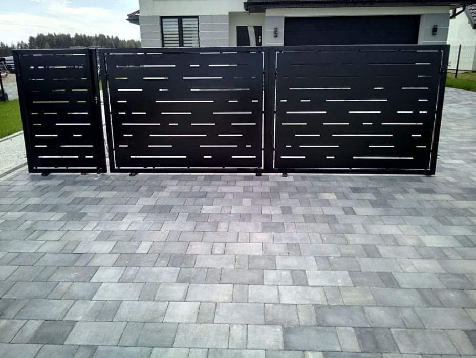 Nowoczesna, czarna brama wjazdowa z poziomymi, prostokątnymi wycięciami, na tle domu z garażem i szarą kostką brukową.