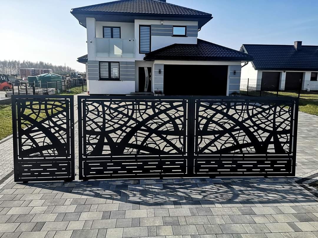 Nowoczesna, czarna brama wjazdowa z ażurowym wzorem na tle dwupiętrowego domu z garażem.