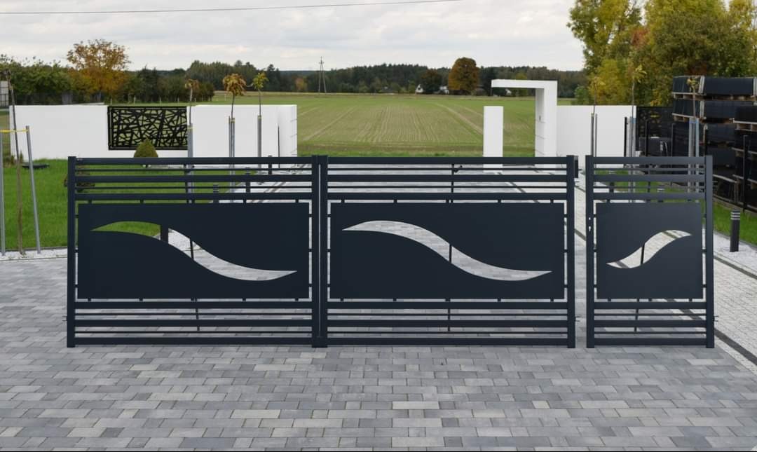 Nowoczesna, metalowa brama wjazdowa z ażurowym wzorem fali na tle zielonego pola i białego muru z dekoracyjnym panelem.