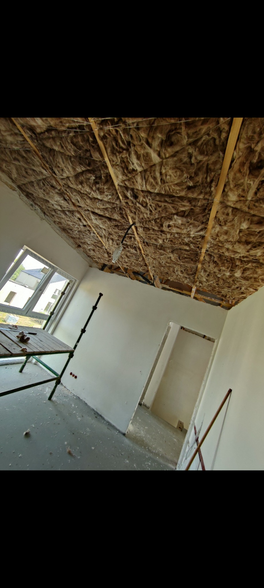 Izolacja termiczna stropu wełną mineralną pomiędzy drewnianymi belkami, widoczne instalacje elektryczne, ściany przygotowane do malowania, rusztowanie w pomieszczeniu.