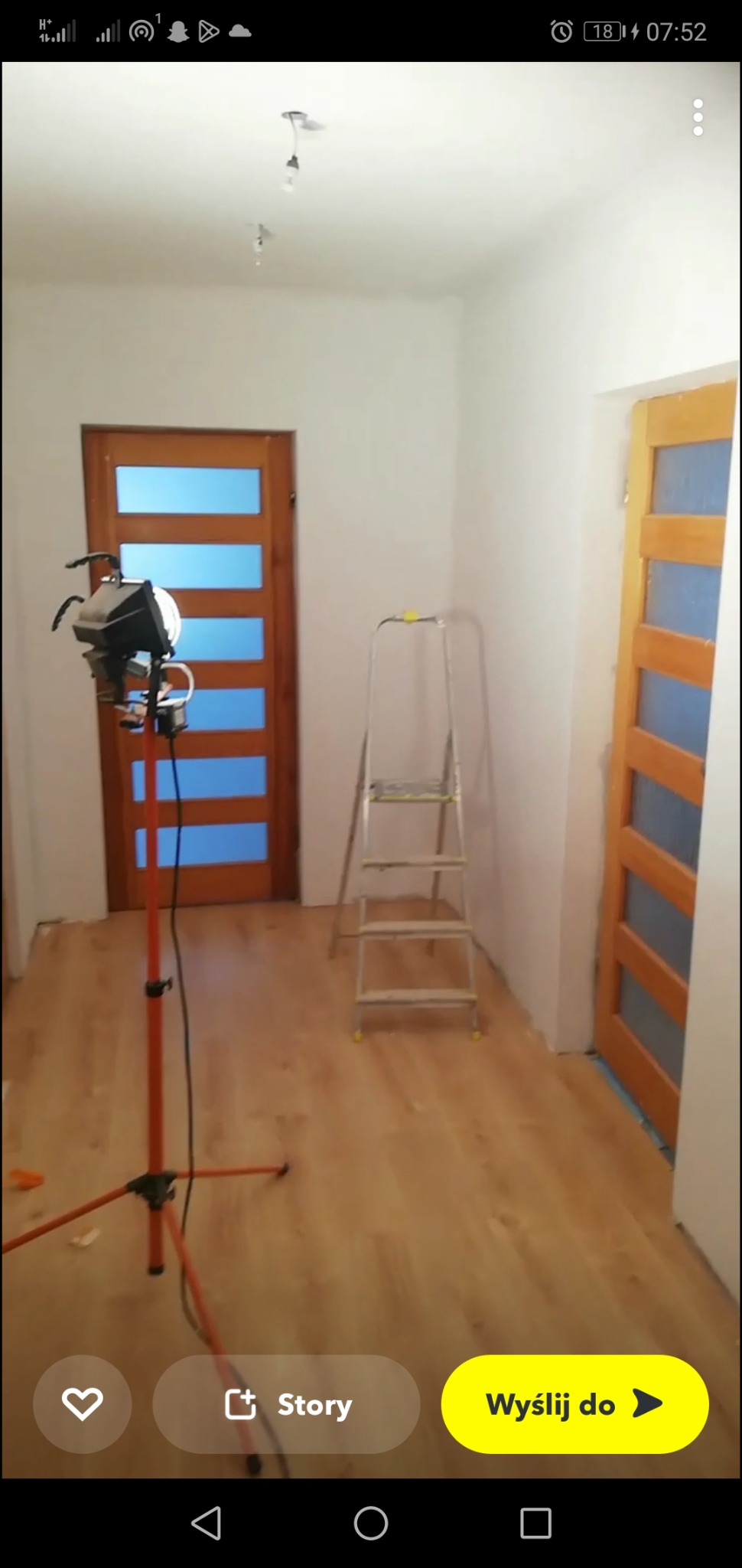 Wnętrze pokoju w trakcie malowania ścian na biało, widoczne dwie drewniane drzwi z szybami, drabina aluminiowa oraz lampa studyjna na statywie.