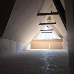 Buw-Koral Karol Brozdowski - Poddasze w trakcie zabudowy: ściany i skośny sufit pokryte płytami gipsowo-kartonowymi, widoczne drewniane elementy konstrukcyjne, surowe wykończenie podłoża.