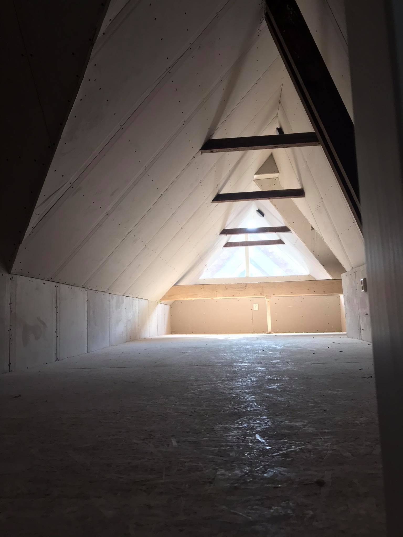Poddasze w trakcie zabudowy: ściany i skośny sufit pokryte płytami gipsowo-kartonowymi, widoczne drewniane elementy konstrukcyjne, surowe wykończenie podłoża.