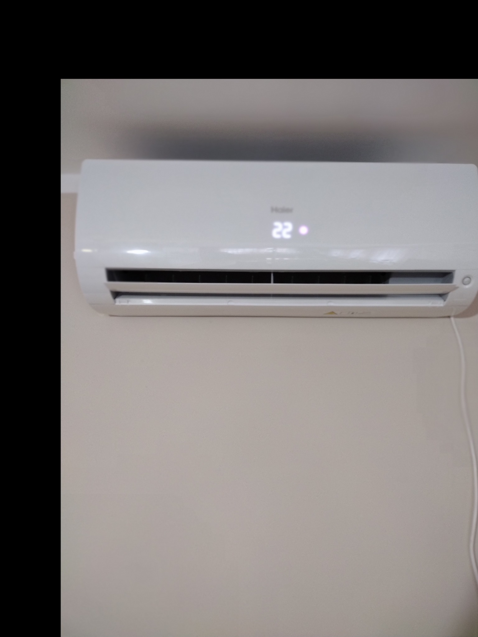 Biała klimatyzacja Haier zamontowana na jasnej ścianie, wyświetlająca temperaturę 22 stopnie Celsjusza.