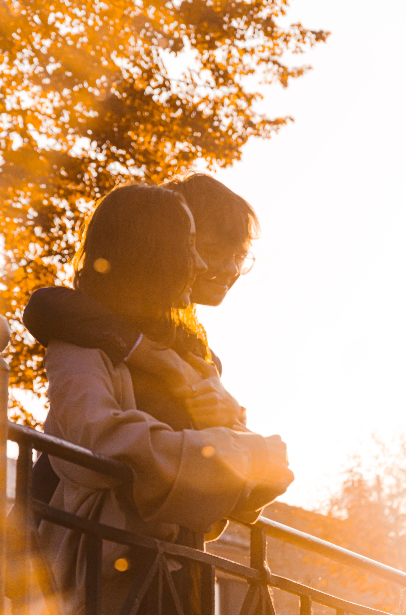 Para narzeczonych w plenerze, obejmująca się przy metalowej barierce, z promieniami zachodzącego słońca w tle, widok od dołu.