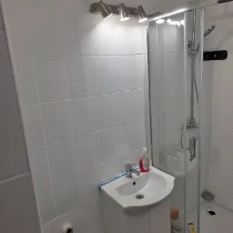 Biała łazienka po malowaniu, z kabiną prysznicową i umywalką. Widoczne świeże białe ściany i drobne niedociągnięcia w wykończeniu.