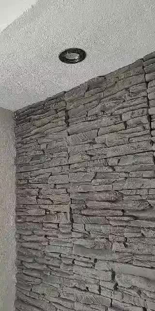 Ściana wykończona szarą okładziną imitującą kamień, z widocznym punktowym oświetleniem sufitowym.