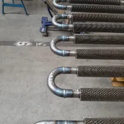 Rzędy rur z żebrowaniem, połączone spawami, leżące na betonowej posadzce; na jednej z rur widoczny napis '1925'.