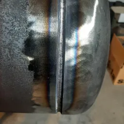 Precyzyjny spaw na metalowej rurze, widoczne tęczowe przebarwienia od ciepła, powierzchnia częściowo pokryta rdzą.