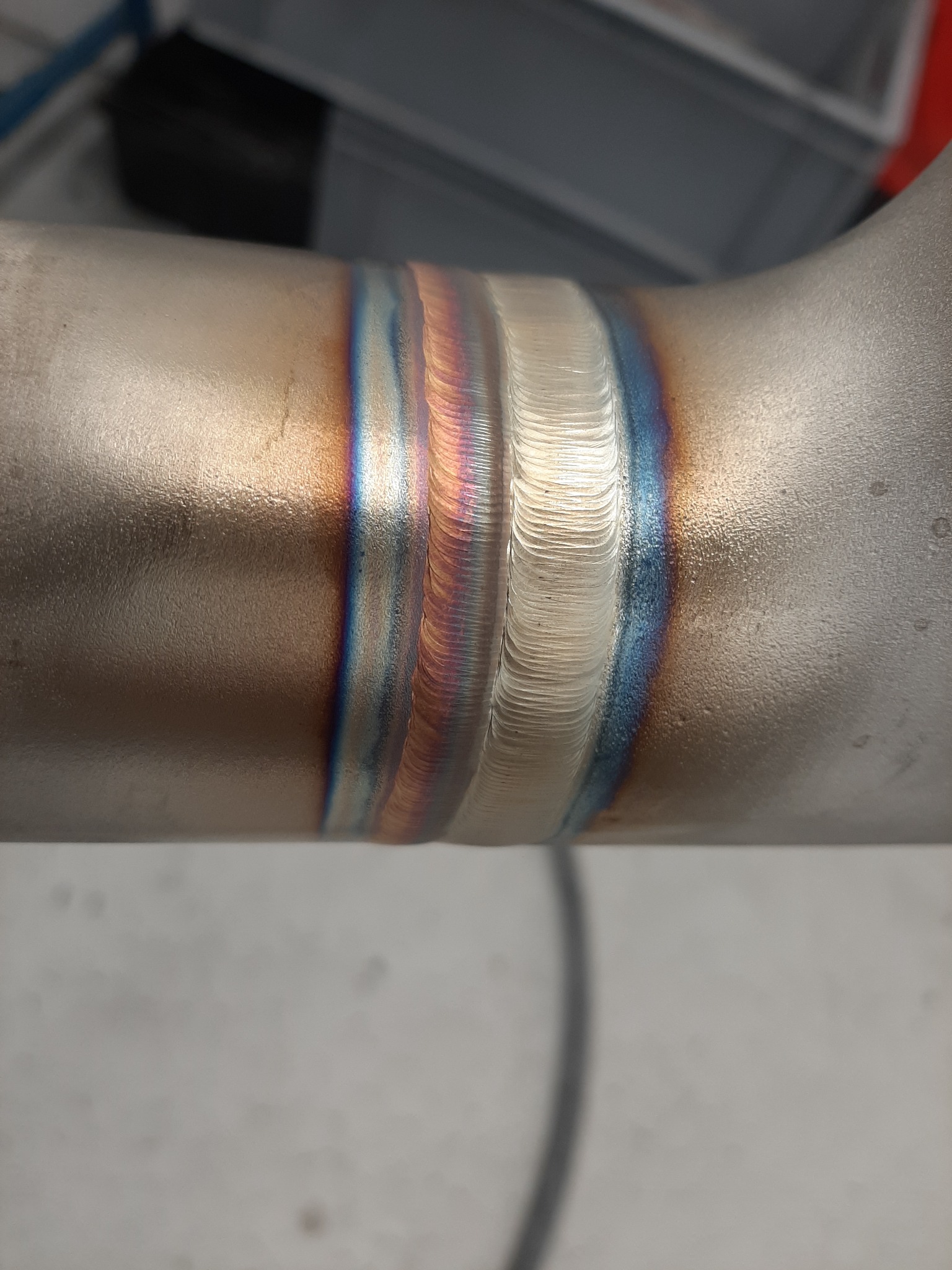 Szczegółowe zbliżenie na spaw na rurze ze stali nierdzewnej, widoczne tęczowe przebarwienia termiczne i precyzyjne ułożenie spoin.