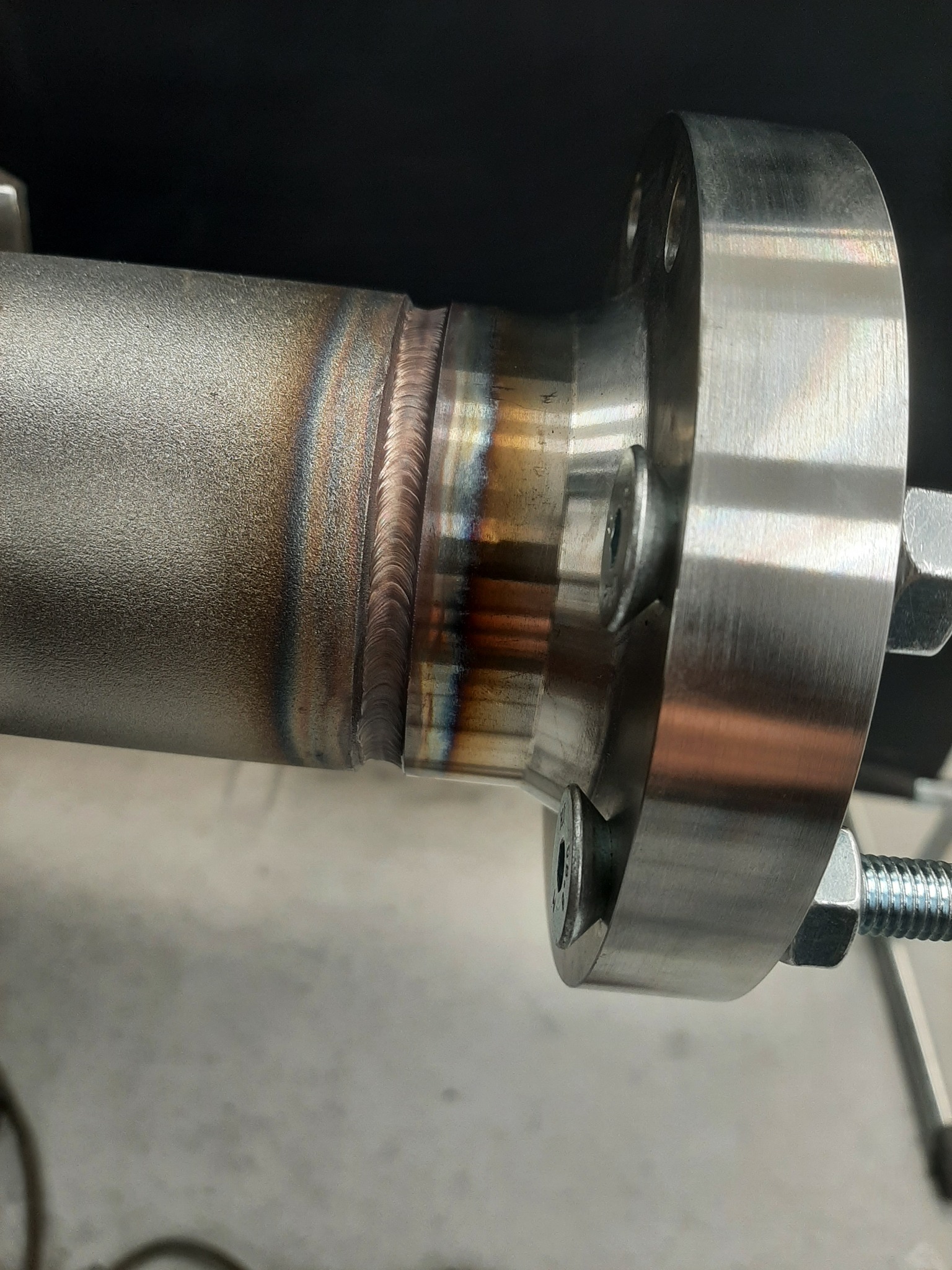 Spoina na rurze ze stali nierdzewnej, widoczne ślady termiczne i precyzyjne wykończenie spoiny, złączona z kołnierzem za pomocą śrub.