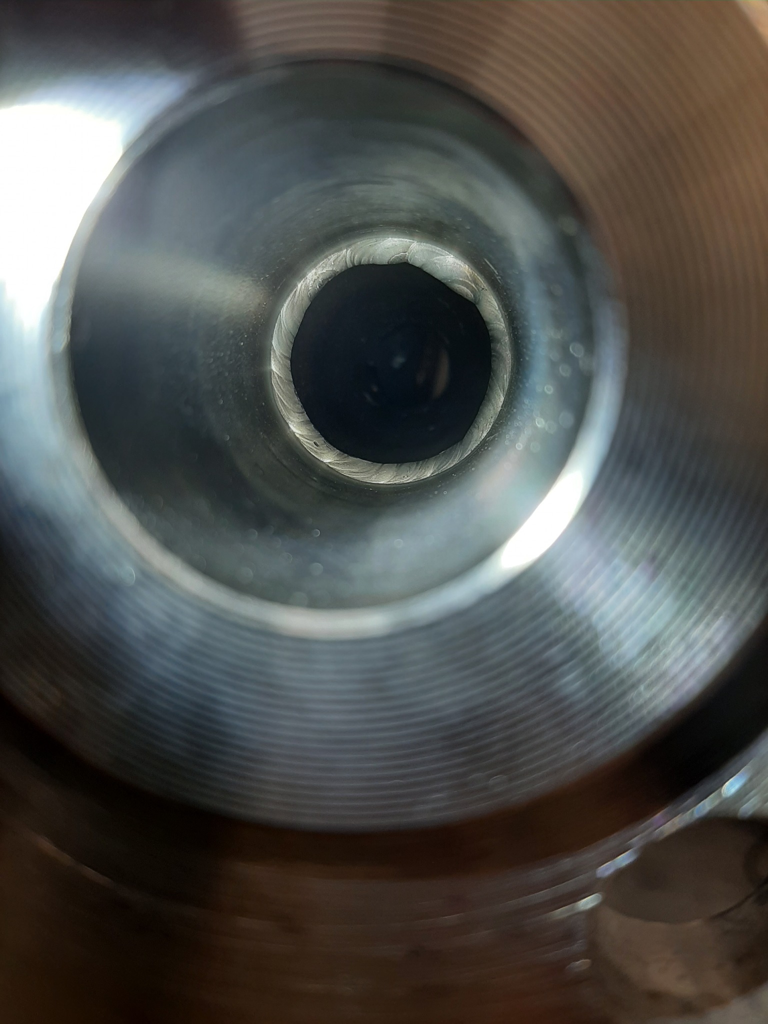 Wnętrze metalowej rury z widocznymi śladami obróbki skrawaniem i delikatnym, spiralnym wzorem na wewnętrznej powierzchni.