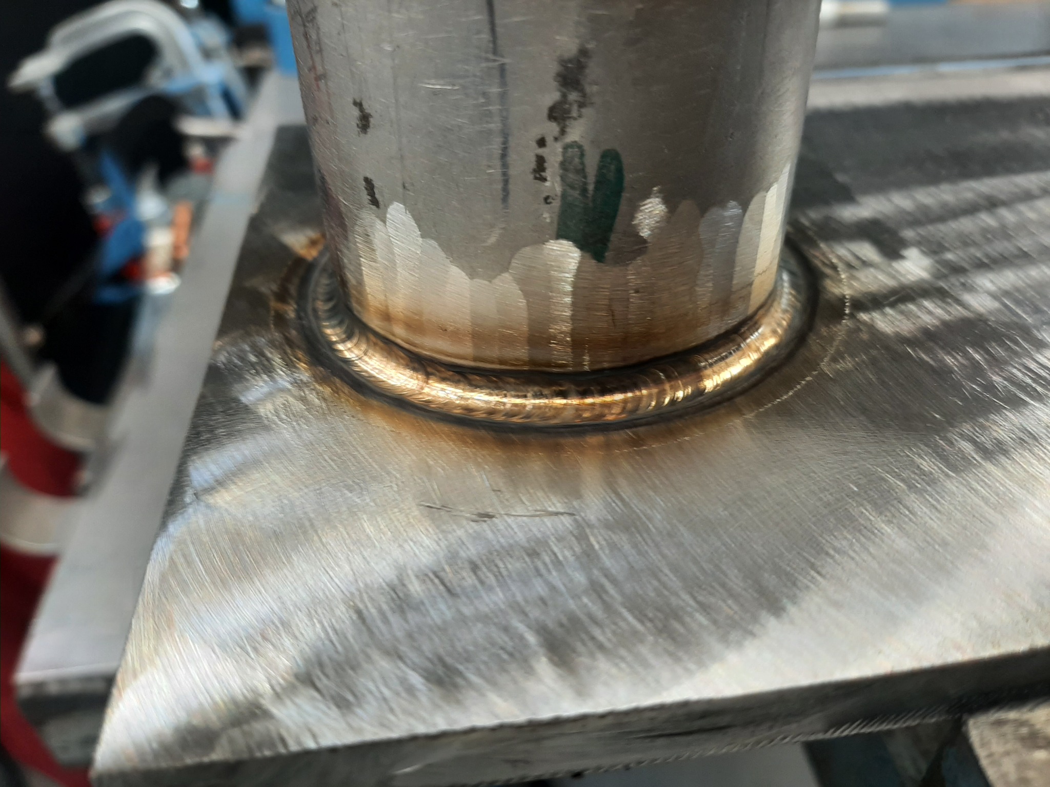 Detal spoiny łączącej okrągły element z płaską powierzchnią metalową, widoczne ślady po procesie spawania i niewielkie zabrudzenia na powierzchni.