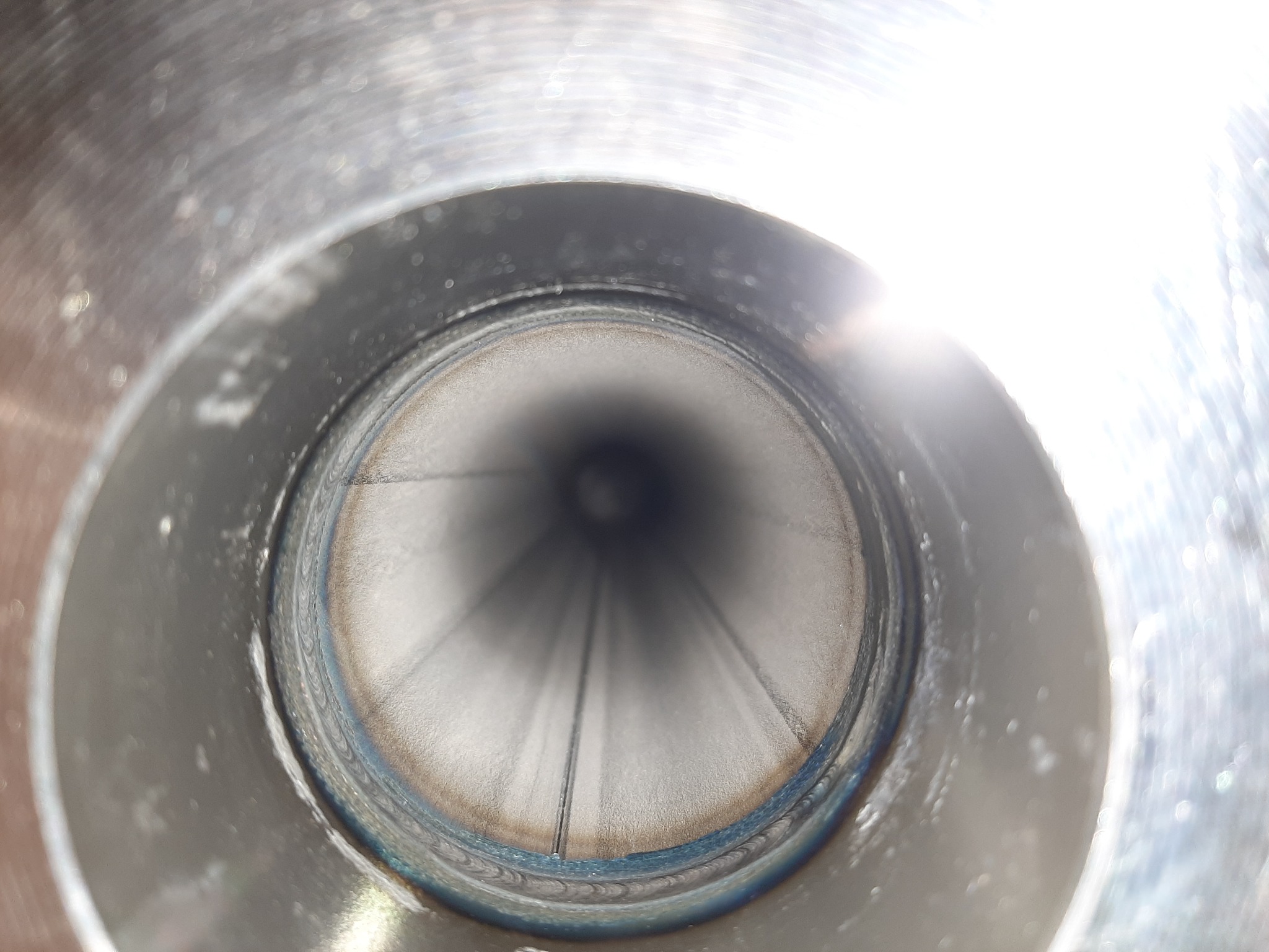 Wewnętrzny widok spawanej rury ze stali nierdzewnej, widoczne ślady po spawaniu i szlifowaniu, oświetlenie od góry.