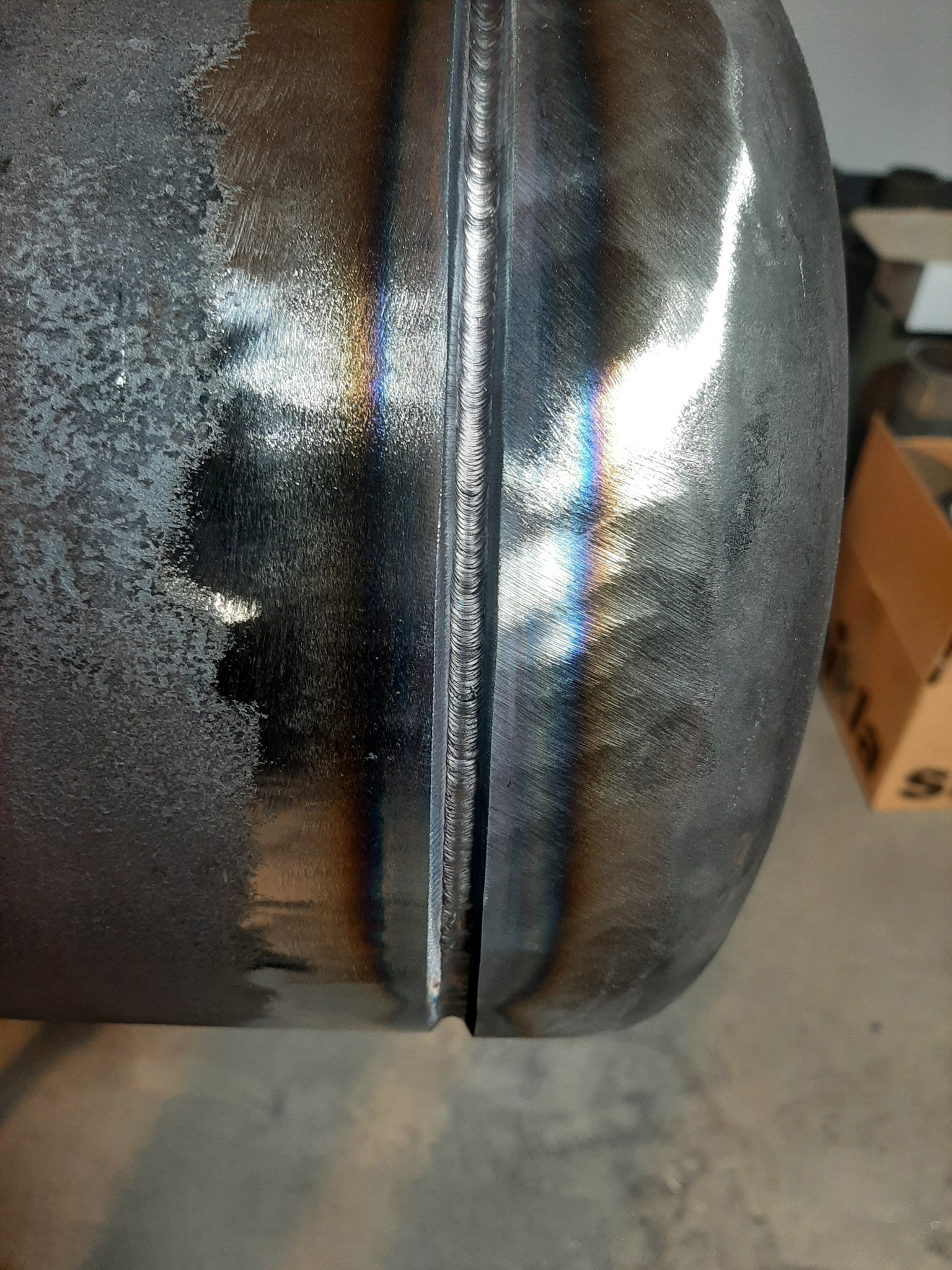 Precyzyjny spaw na metalowej rurze, widoczne tęczowe przebarwienia od ciepła, powierzchnia częściowo pokryta rdzą.