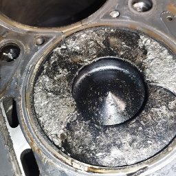 CarService- Dominik Muszkieta - Zablokowany tłok w cylindrze silnika samochodowego, widoczne nagromadzenie nagaru i osadów, metalowa powierzchnia z widocznymi śladami korozji.