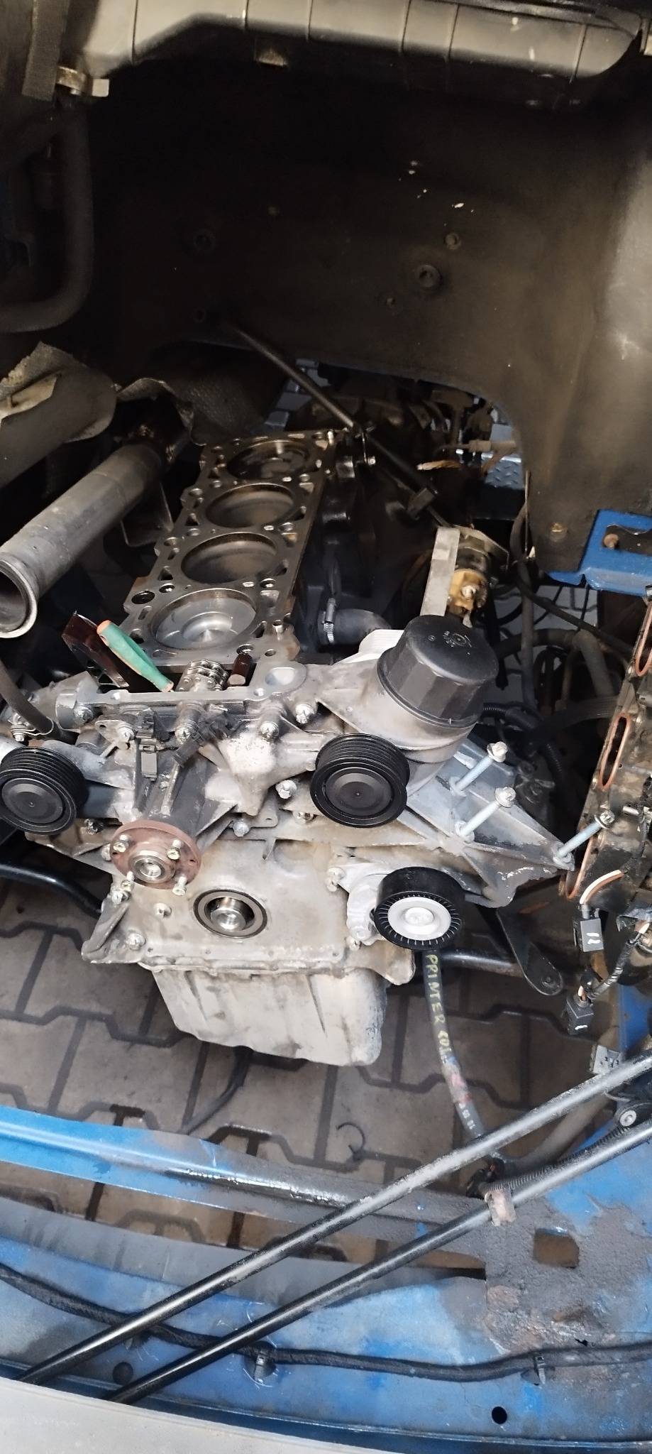 Silnik samochodowy w trakcie naprawy, widoczne elementy wewnętrzne, głowica cylindrów z otworami, pasek rozrządu i inne podzespoły, tło nieostre.