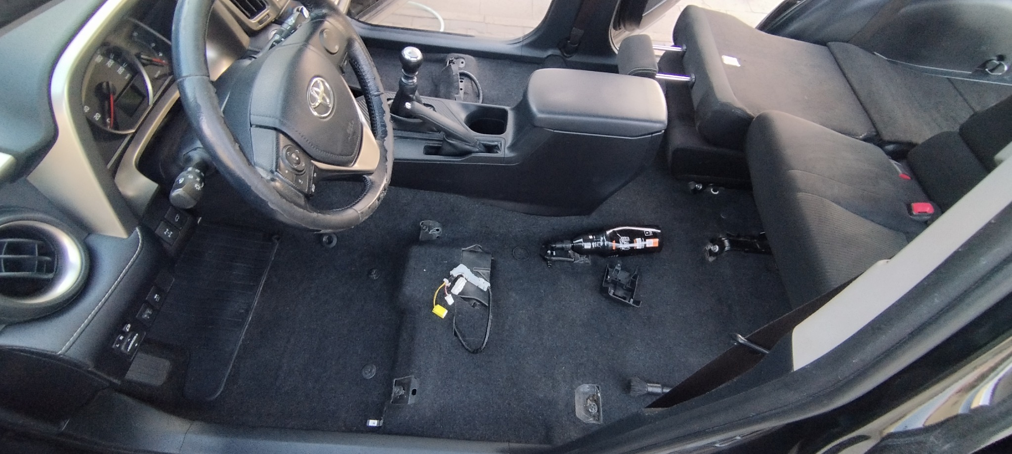 Wnętrze samochodu Toyota Rav4 zdemontowane do czyszczenia; widoczne odsłonięte mocowania foteli, panel sterowania, kierownica i elementy demontażu na dywaniku.