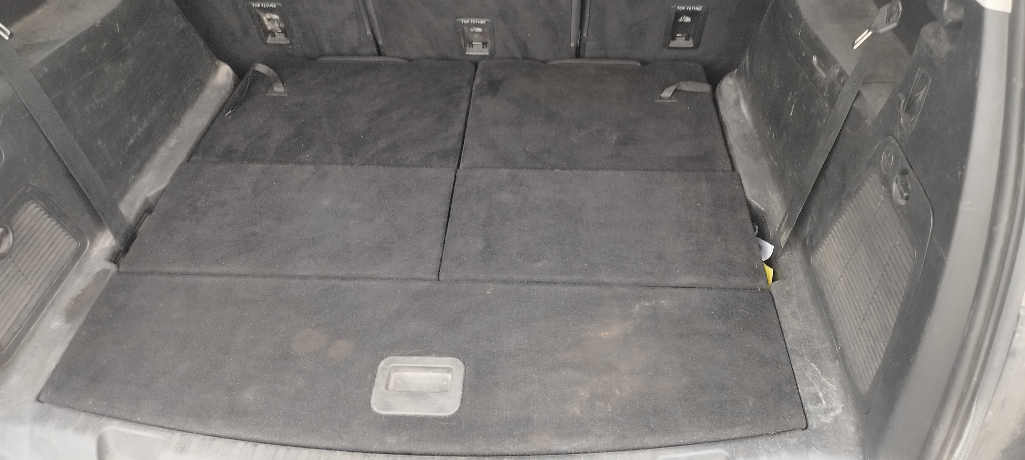 Pusta, czarna przestrzeń bagażowa samochodu typu van z trzema składanymi panelami podłogowymi i uchwytami mocującymi na ścianach bocznych.