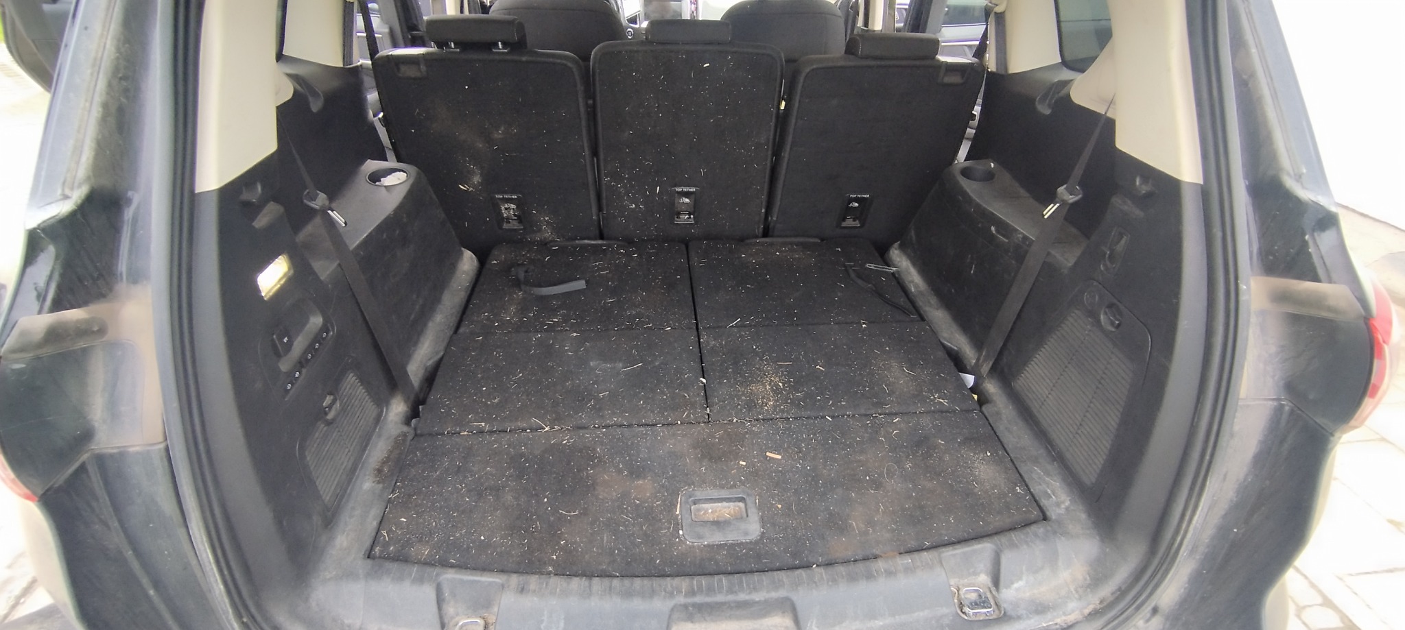 Wnętrze bagażnika SUV-a w widoku od tyłu, z widocznymi złożonymi siedzeniami i zabrudzeniami na wykładzinie.