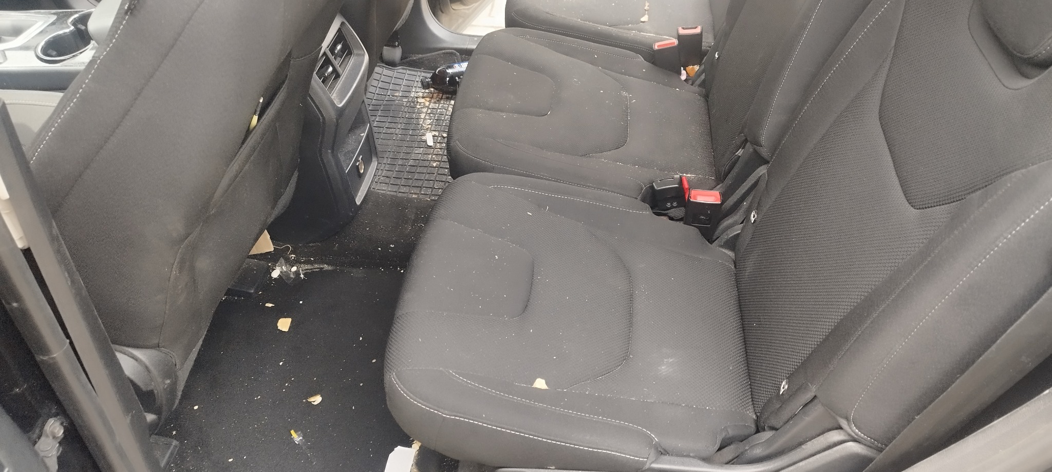 Wnętrze samochodu z widocznymi tylnymi siedzeniami i podłogą, na których widać liczne zabrudzenia i resztki jedzenia.