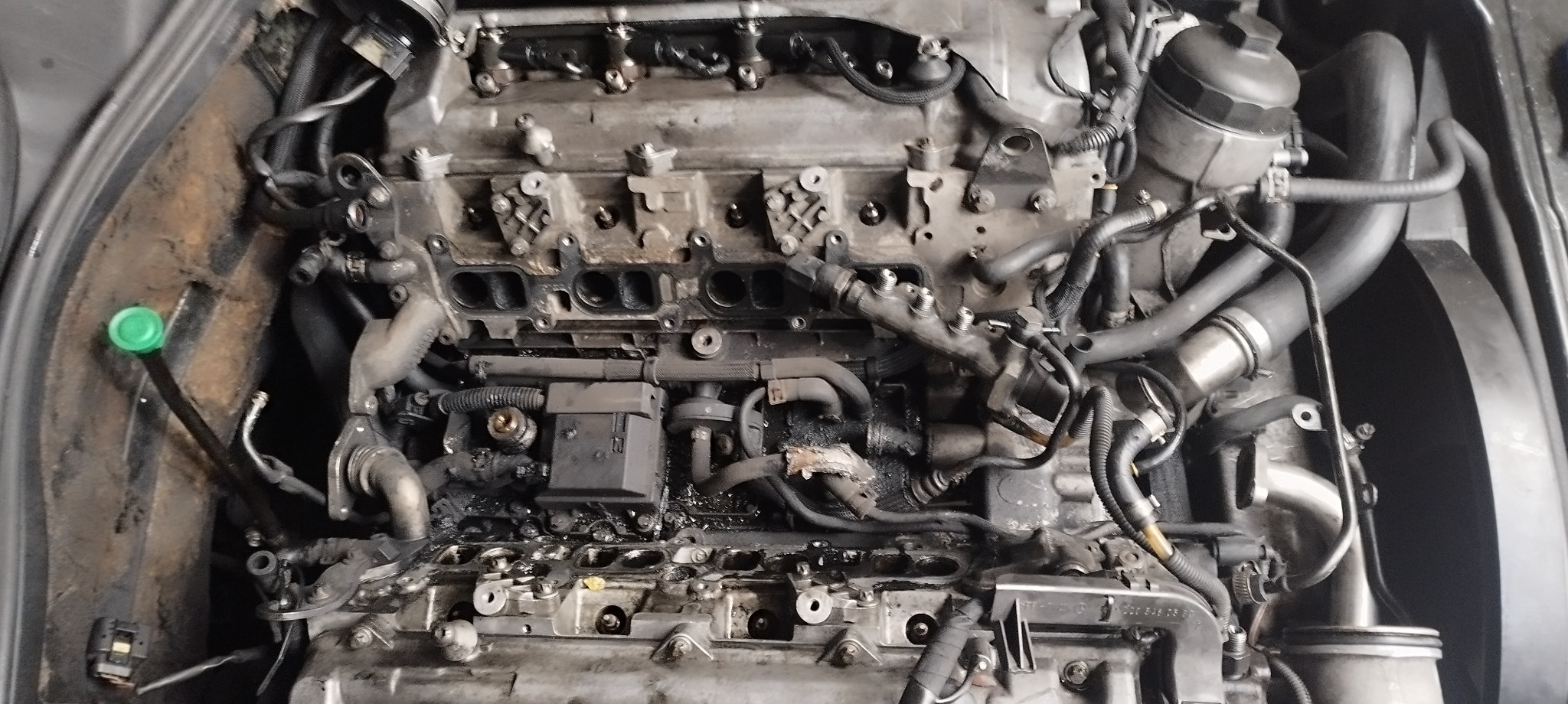 Widok z góry na silnik samochodowy w trakcie naprawy, z widocznymi elementami układu dolotowego i wtryskowego, z zielonym korkiem na przewodzie po lewej stronie.