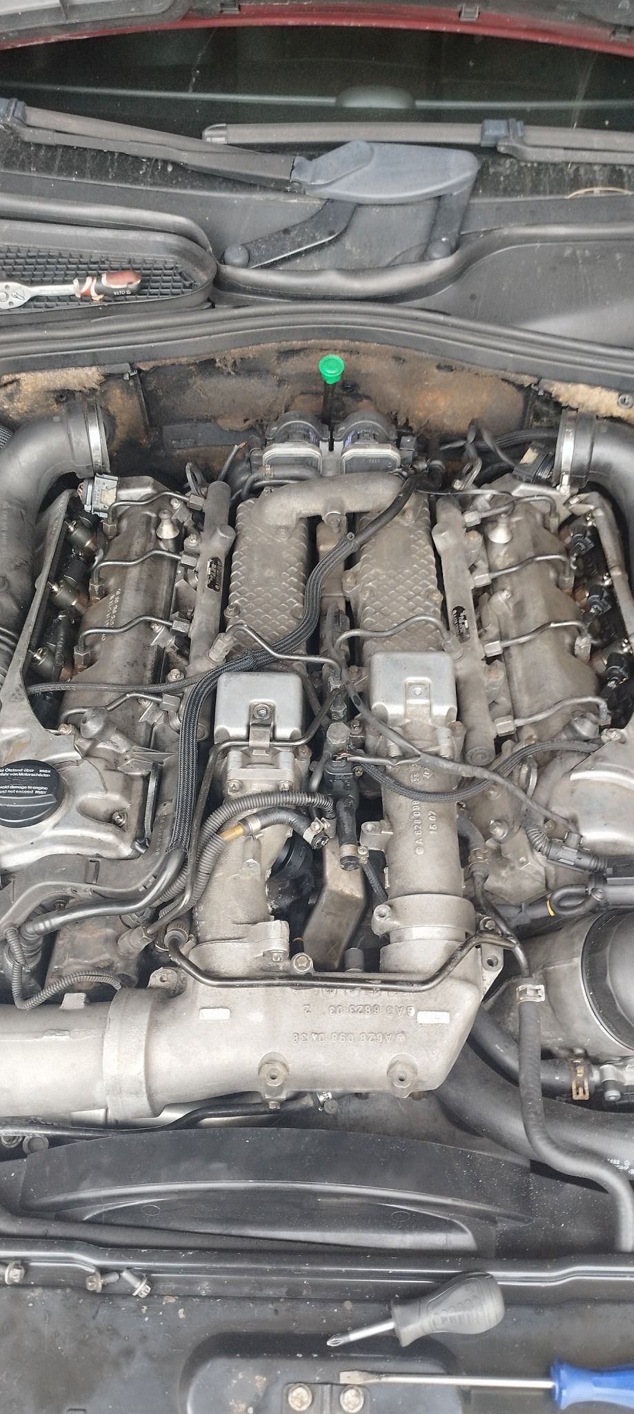 Widok na silnik samochodowy z widocznymi przewodami, wtryskiwaczami i innymi podzespołami, z dwoma śrubokrętami leżącymi na dole zdjęcia.