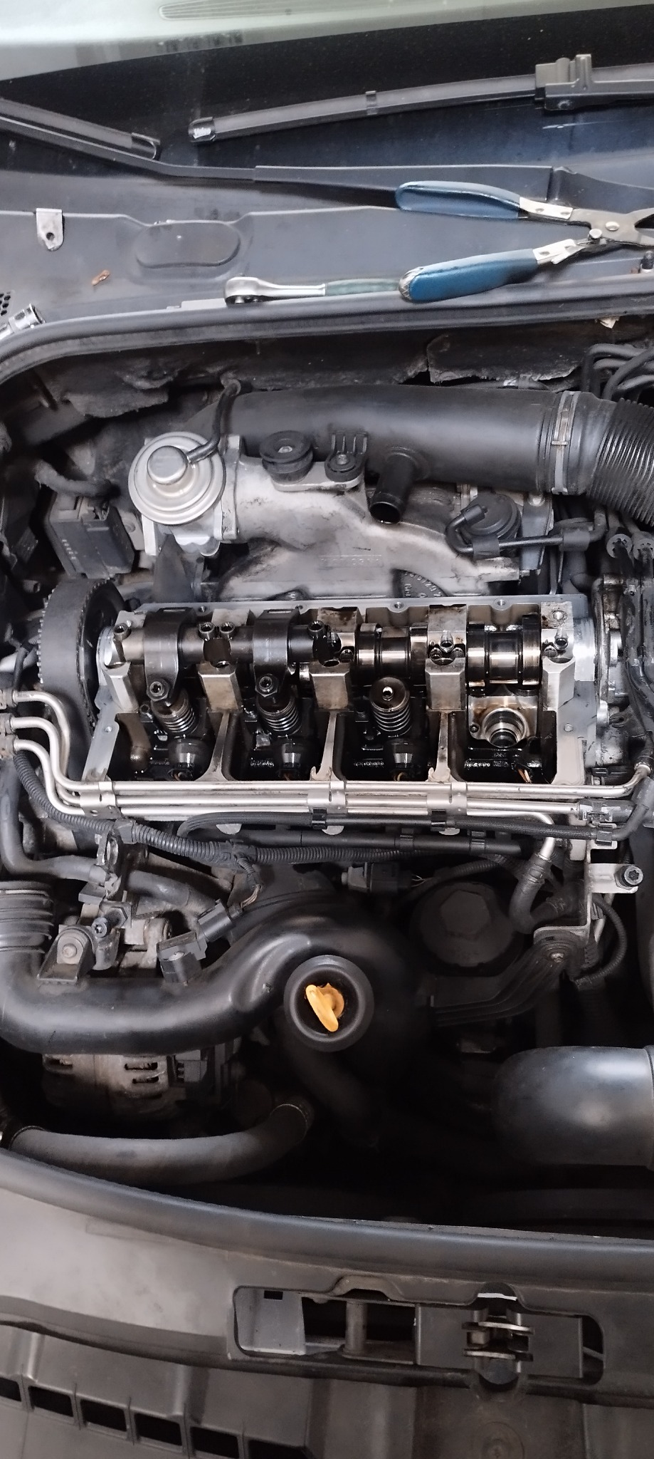 Otwarty silnik samochodowy z widocznymi wałkami rozrządu, sprężynami zaworowymi i narzędziami (szczypce, klucz) w tle.