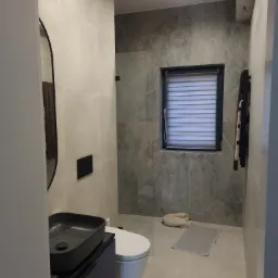 Nowoczesna łazienka z szarymi płytkami imitującymi marmur, wiszącą toaletą i umywalką nablatową w kolorze antracytowym, z minimalistycznym oświetleniem punktowym.