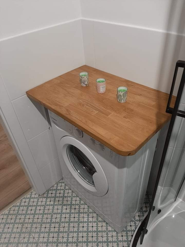 Pralka z blatem drewnianym w łazience z płytkami w stylu retro i trzema świeczkami zapachowymi na blacie.