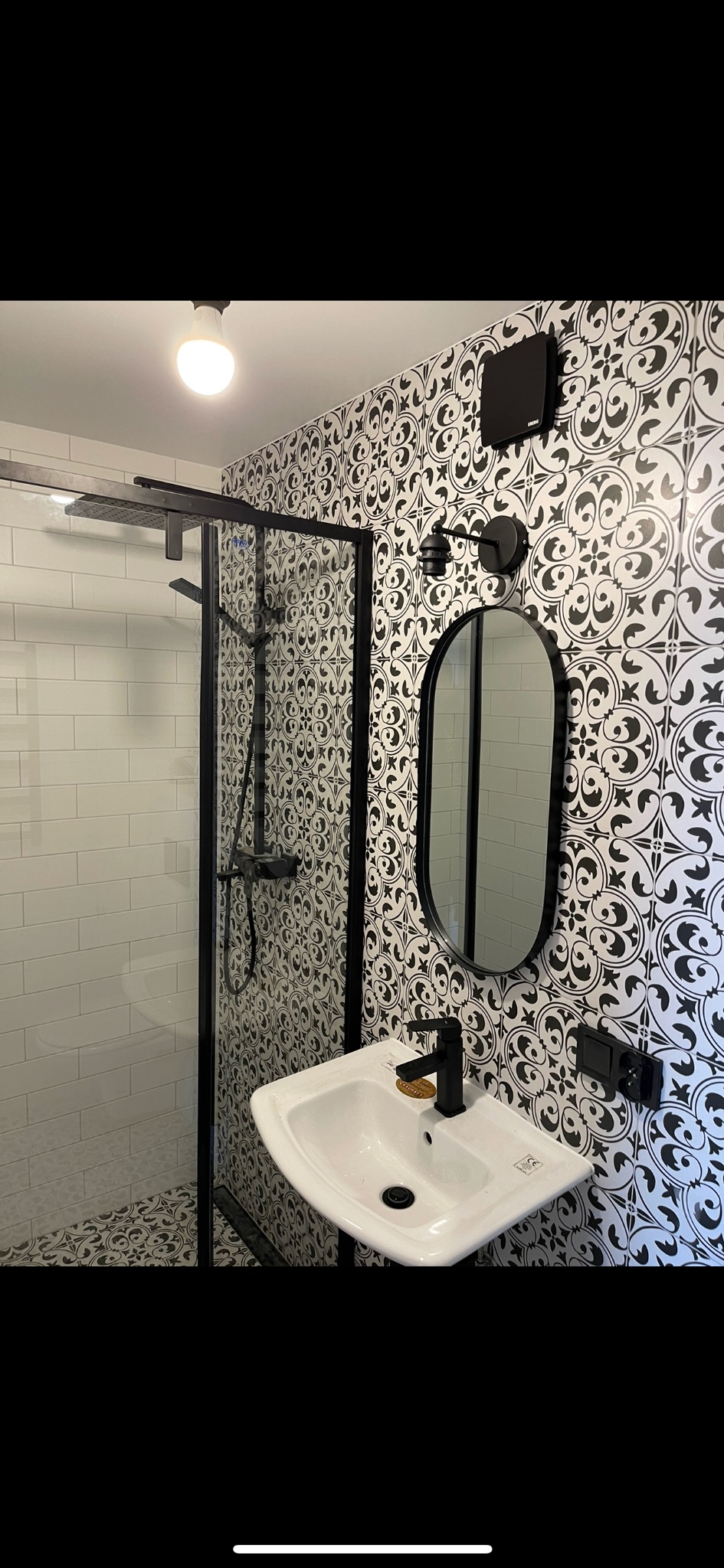 Nowoczesna łazienka z kabiną prysznicową typu walk-in, umywalką nablatową i czarno-białymi płytkami z motywem ornamentów.