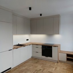 MEBLE TTR TOMASZ TRZEŚNIOWSKI - Jasna kuchnia na wymiar z drewnianym blatem i czarnymi akcentami, widok na parkiet w jodełkę.