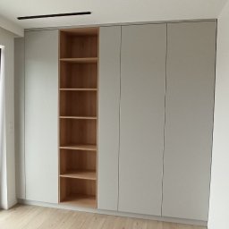 MEBLE TTR TOMASZ TRZEŚNIOWSKI - Szara szafa wnękowa z drewnianymi półkami, widok na jasną podłogę i fragment kosza na pranie.