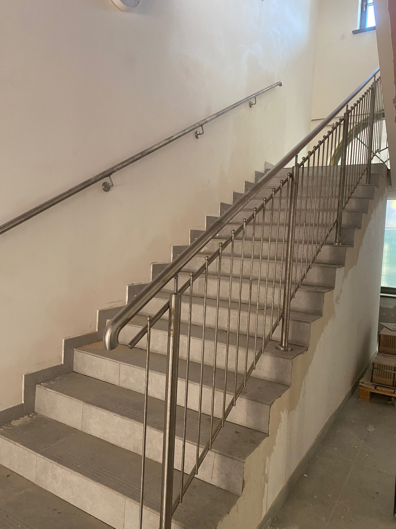 Wnętrze klatki schodowej w Lubsku z metalowymi schodami i prostą, nierdzewną balustradą oraz poręczą, w trakcie wykańczania.