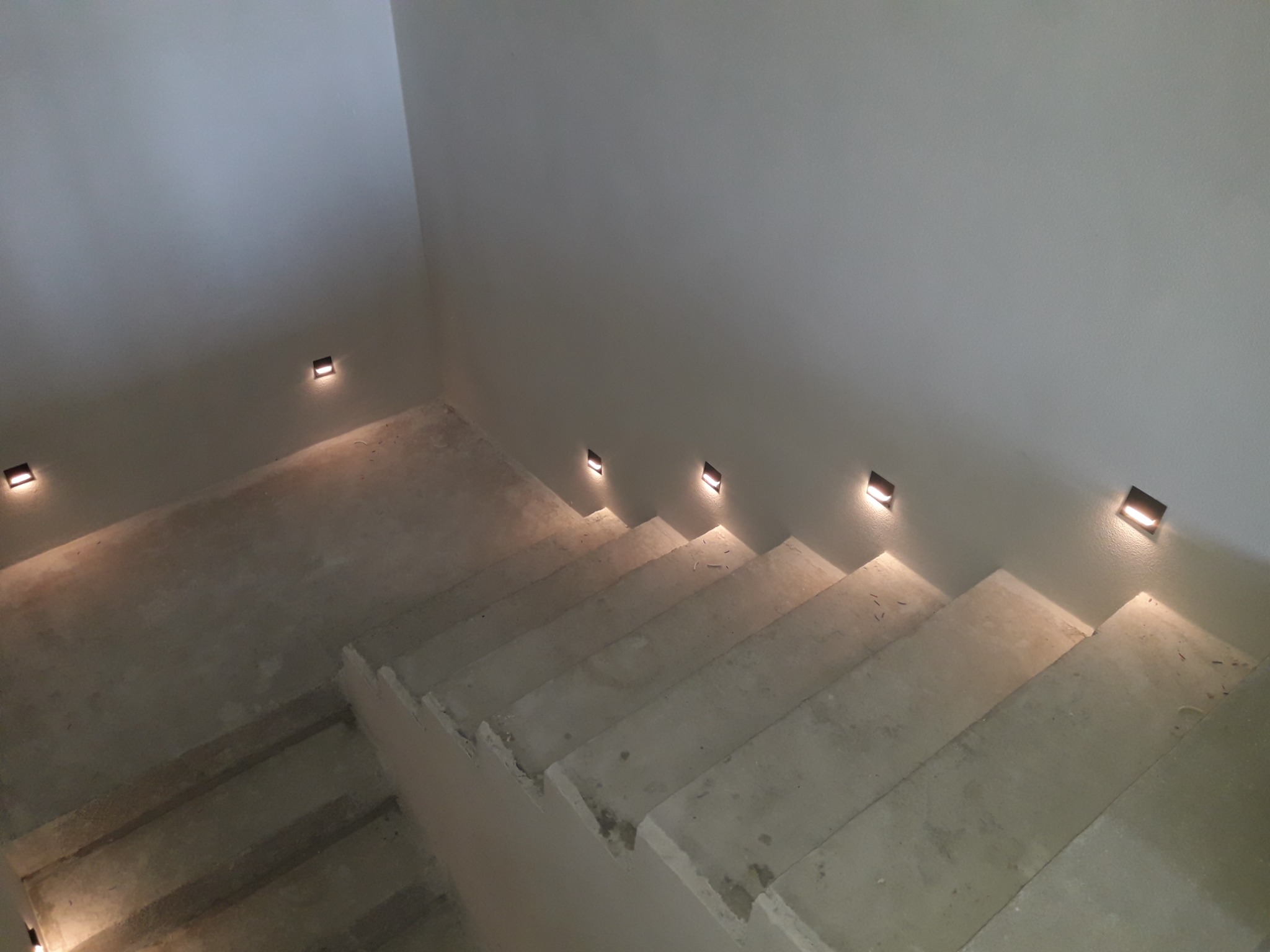 Schody betonowe z wbudowanym oświetleniem LED w ścianie, minimalistyczny design.