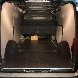 Wnętrze pustej furgonetki z wyłożoną podłogą i ścianami, przygotowanej do transportu towar&oacute;w, z małym kartonem z tyłu.