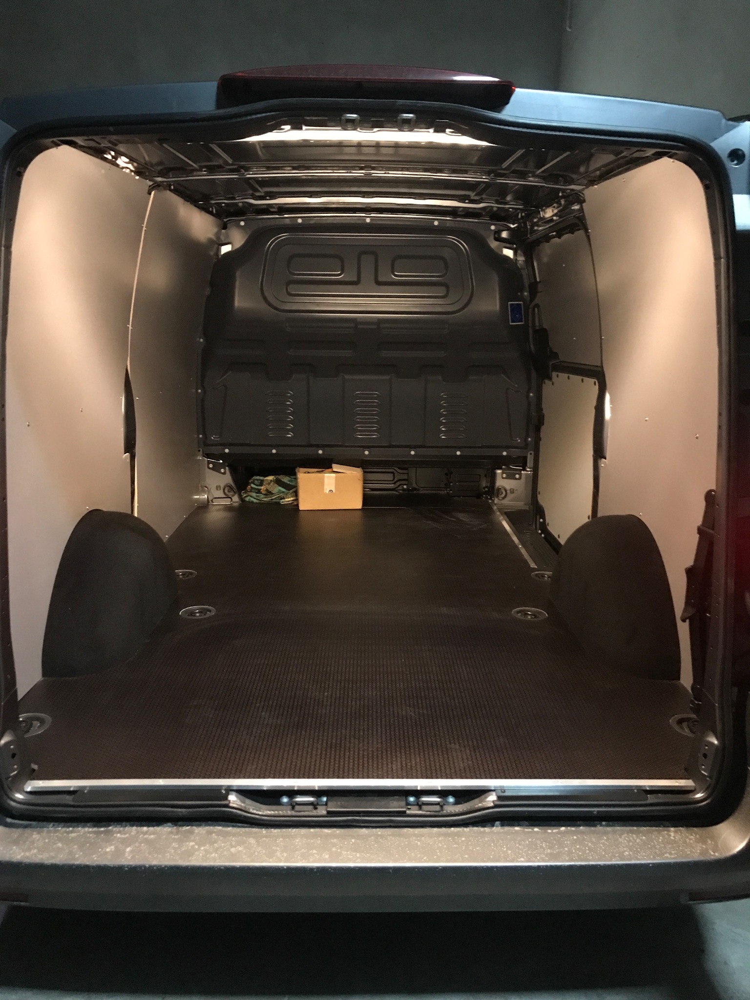 Wnętrze pustej furgonetki z wyłożoną podłogą i ścianami, przygotowanej do transportu towarów, z małym kartonem z tyłu.