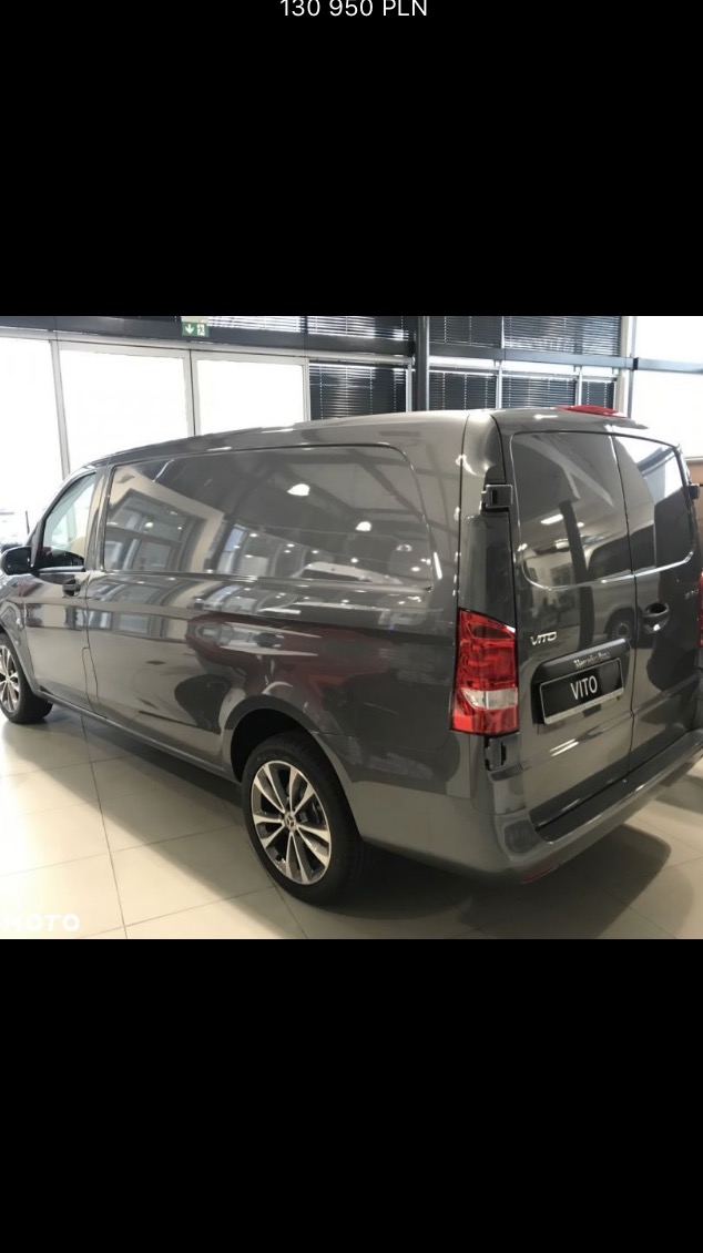 Szary samochód dostawczy Mercedes Vito, widok z tyłu, zaparkowany w salonie samochodowym z ceną w rogu zdjęcia.