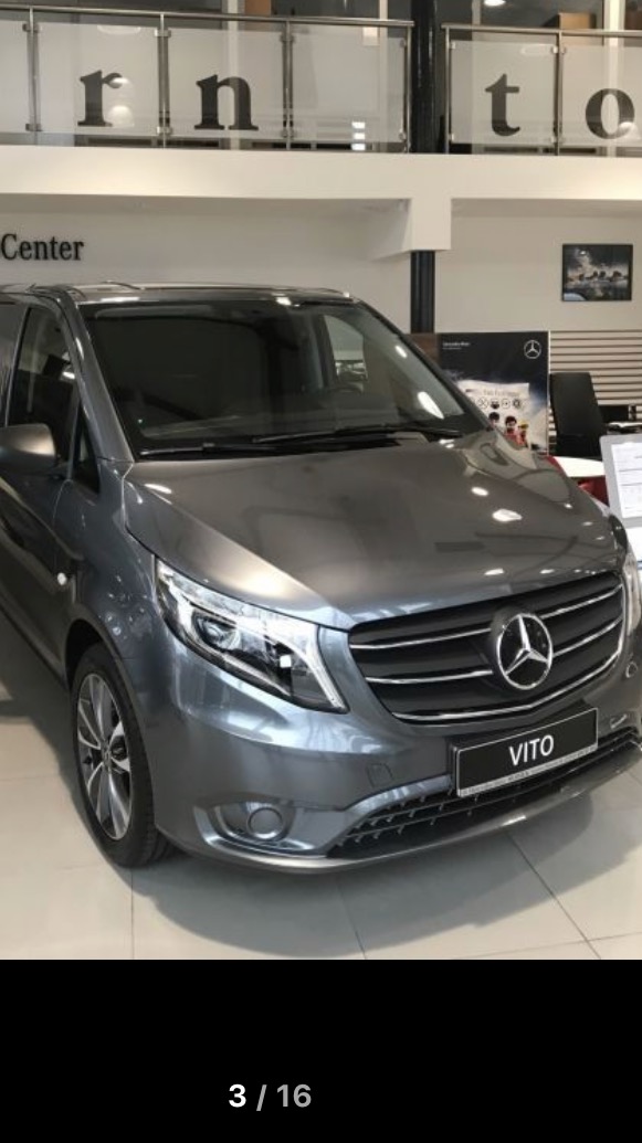 Szary Mercedes-Benz Vito zaparkowany w salonie samochodowym, widok z przodu na reflektory i grill z logo Mercedes-Benz.