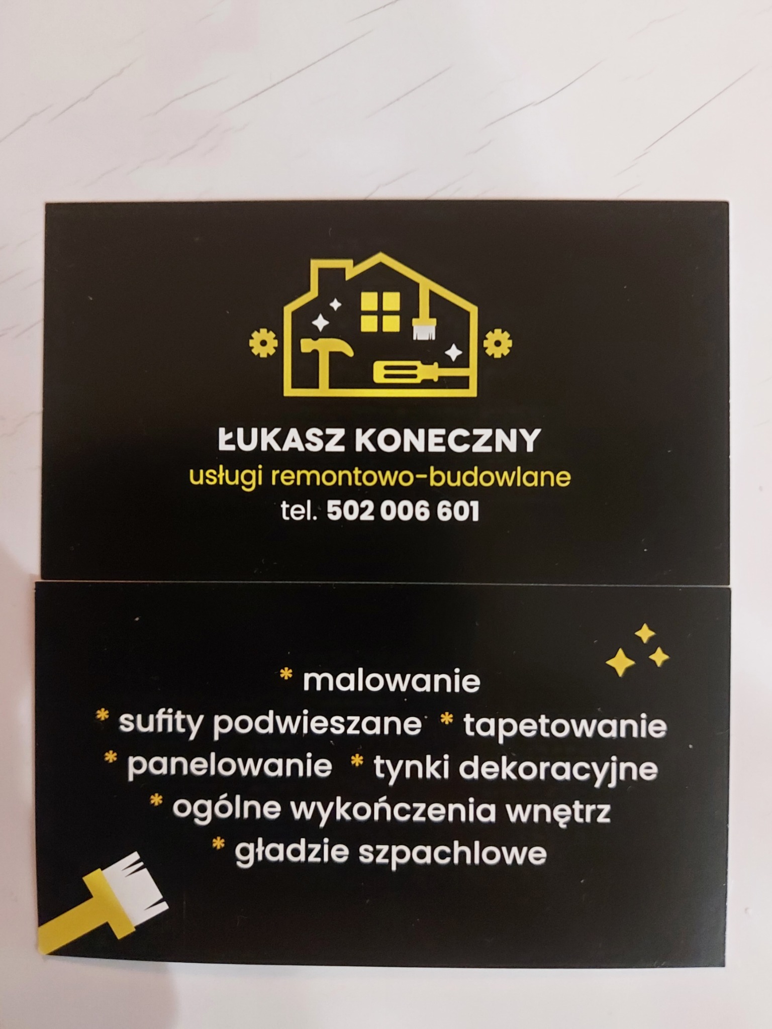 Wizytówka firmy Łukasz Koneczny oferującej usługi remontowo-budowlane, z logo przedstawiającym dom z narzędziami i listą usług: malowanie, sufity podwieszane, tapetowanie, panelowanie, tynki...
