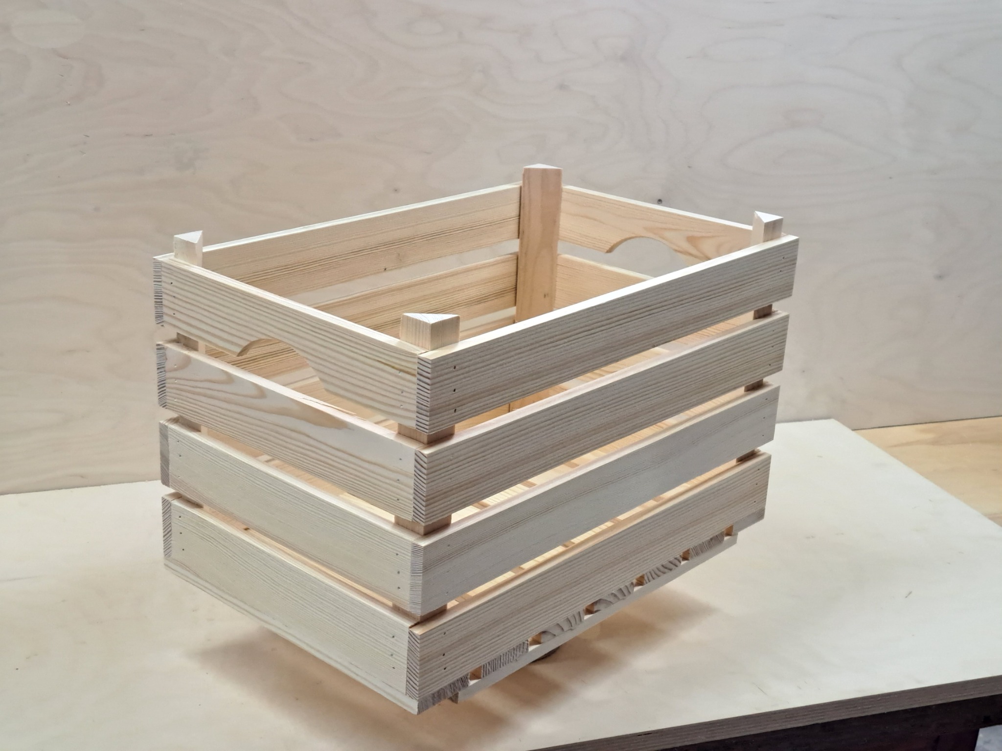 Surowa, jasna skrzynka z drewna sosnowego, widoczne ślady po zszywkach, stojąca na drewnianym blacie.