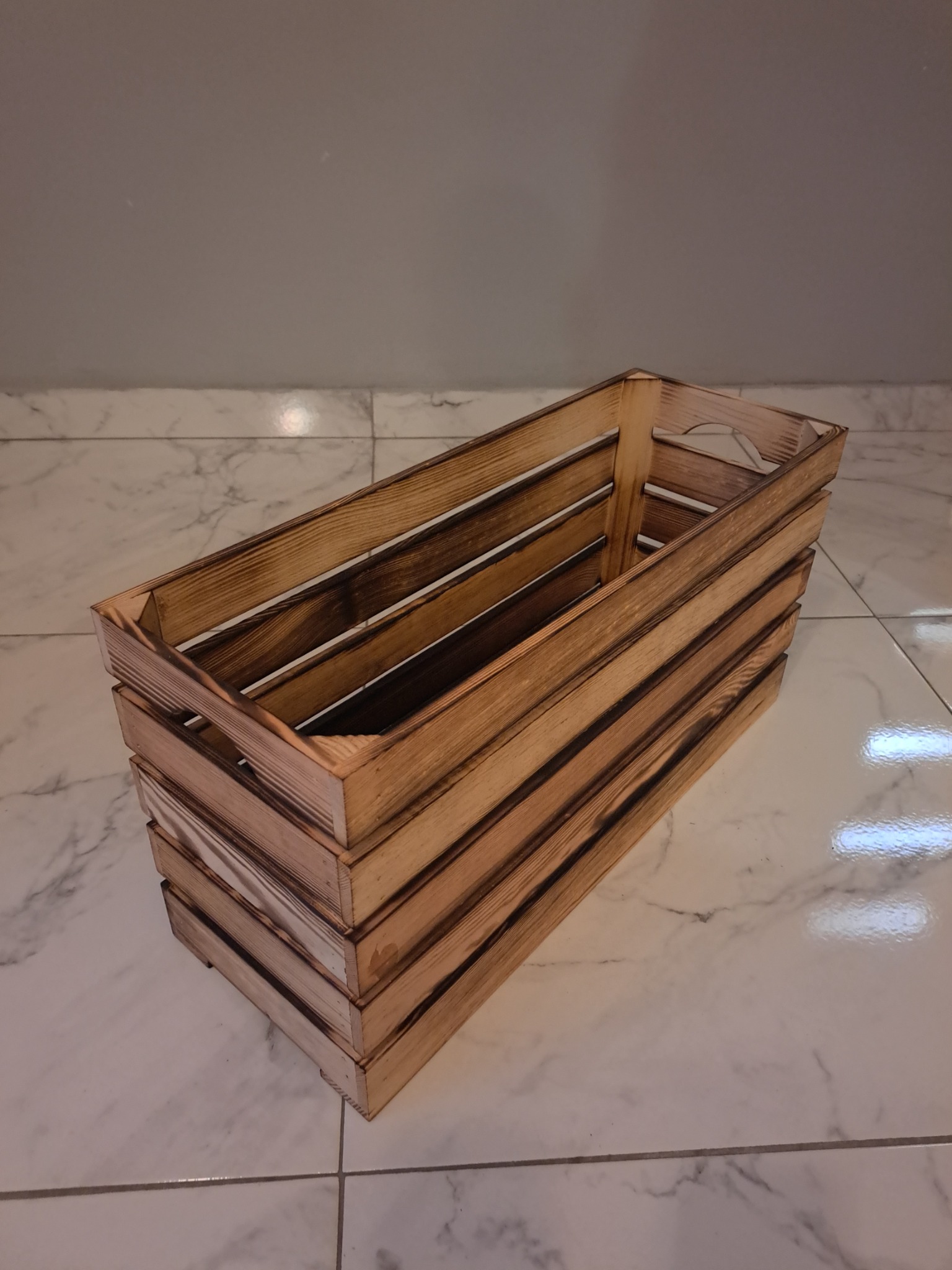 Drewniana skrzynka z opalonymi brzegami, ustawiona na marmurowej podłodze.
