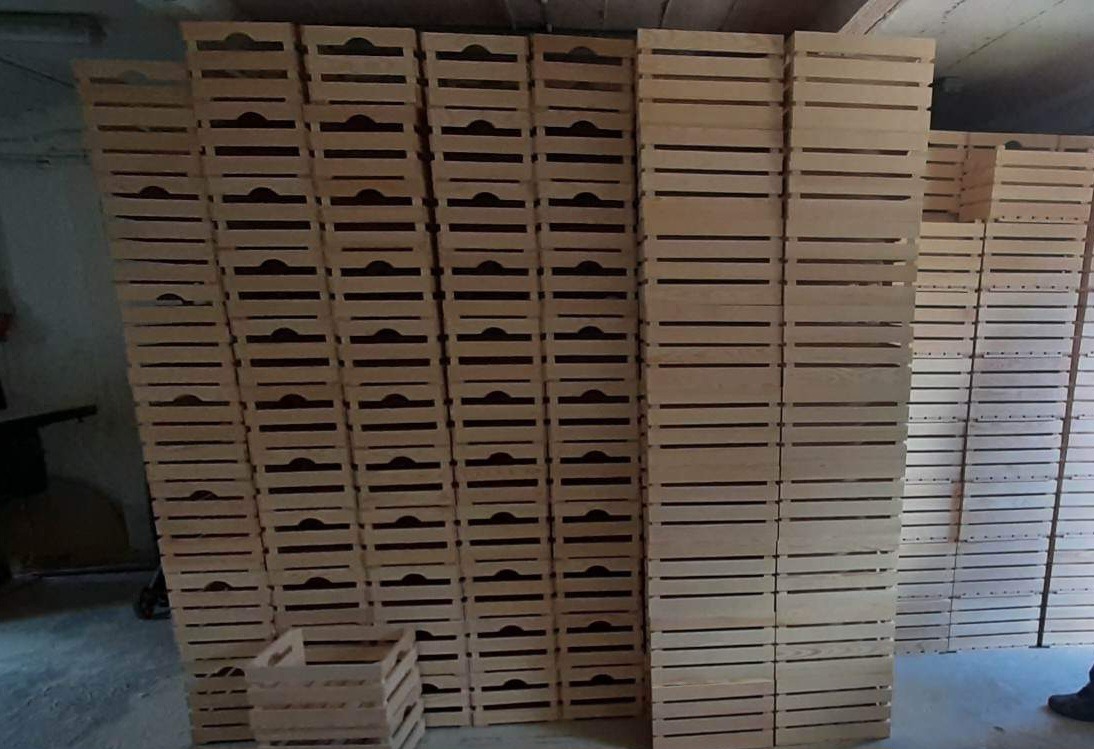 Stos skrzynek drewnianych w warsztacie, z widocznymi szczelinami i uchwytami, jedna skrzynka na pierwszym planie.