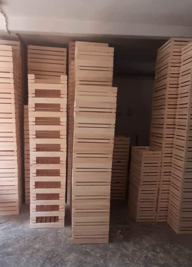 Stosy surowych, drewnianych skrzynek magazynowych, ustawionych w rzędach w słabo oświetlonym pomieszczeniu.